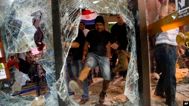 Un hombre da una patada a una ventana rota del edificio del congreso durante los enfrentamientos entre la policía y los manifestantes que se oponen a una enmienda constitucional aprobada que permitiría la elección de un presidente a un segundo mandato, en Asunción, Paraguay, el 31 de marzo de 2017.
