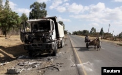 FILE - A man drives a horse-cart past the wreckage of a truck torched during recent demonstrations along the road in Holonkomi town, in Oromia region of Ethiopia, Dec. 17, 2015.