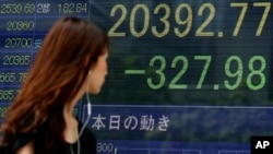 A woman walks past an electronic stock indicator of a securities firm in Tokyo, displaying Tokyo’s Nikkei 225 that lost 327.98 points or 1.58 percent to 20,392.77, Wednesday, Aug. 12, 2015. 