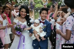 Bride Amornrat Ruamsin (L), 27, who is a transgender, holds up her five-month-old daughter with her groom Pitchaya Kachainrum (R), 16, during their wedding ceremony organised by a local TV show, in Bangkok, Thailand, Feb. 9, 2018.
