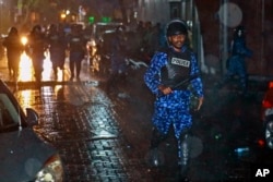 A Maldives policeman charges with baton towards protesters after the government declared a 15-day state of emergency in Male, Maldives, early Tuesday, Feb. 6, 2018.