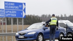Seorang polisi menghentikan kendaraan untuk pemeriksaan dokumen di pos kendali lalu lintas, di Lapinjarvi, Finlandia. Arus kendaraan menuju Helsinki dibatasi untuk mencegah penyebaran penyakit corona. 
