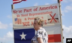 Pamela Taylor, whose home is on the south side of the border fence, stands near a sign she erected, in Brownsville, Texas.