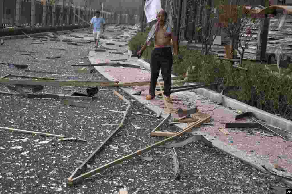 Um homem perto de vidros no chão após a explosão ter quebrado janelas num bairro residencial, em Tianjin, China, Quinta-feira, 13 de Agosto, 2015.&nbsp; &nbsp;