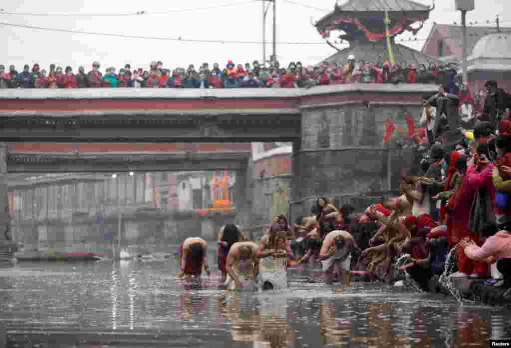 Devotees take a holy bath at Bagmati River in Pashupatinath Temple during the Swasthani Brata Katha festival in Kathmandu, Nepal.