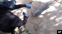 In this image taken from amateur video posted online, appearing to show a presumed UN staff member measuring and photographing a canister in the suburb of Moadamiyeh in Damascus, Syria, Aug. 26, 2013.