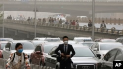 People wearing face masks walk past cars clogged with heavy traffic on a road as Beijing, China, is hit by polluted air and sandstorm, May 4, 2017. 