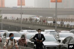 People wearing face masks walk past cars clogged with heavy traffic on a road as Beijing is hit by polluted air and sandstorm, May 4, 2017. Authorities in Beijing issued a blue alert on air pollution as sandstorm swept through the Chinese capital city on Thursday.