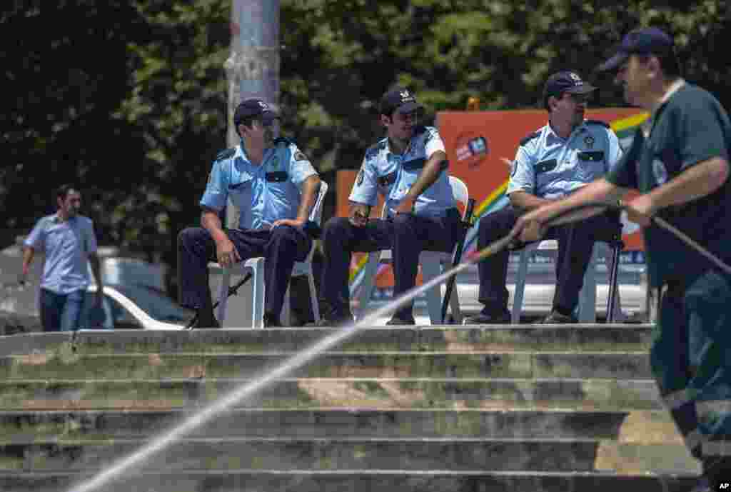 Beberapa orang polisi duduk-duduk di Taman Gezi, Istanbul, sementara seorang pekerja membersihkan daerah itu (17/6).