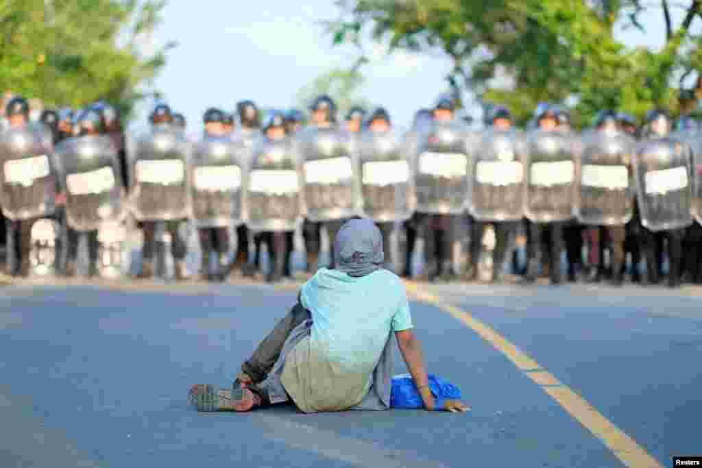 A migrant from Central America sits on a road in front of a Guatemalan police officers after a migrant caravan was blocked by Guatemalan authorities, near the border with Honduras outside of Puerto Barrios, Jan. 16, 2022.