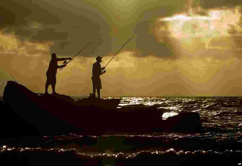Two rmen goes fishing off a jetty as the sun rises in Bal Harbor, Florida.