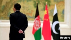 FILE - A member of the security personnel stands guard next to, from left, Afghan, Chinese and Pakistani flags during the first China-Afghanistan-Pakistan Foreign Ministers' Dialogue in Beijing, China, Dec. 26, 2017. 