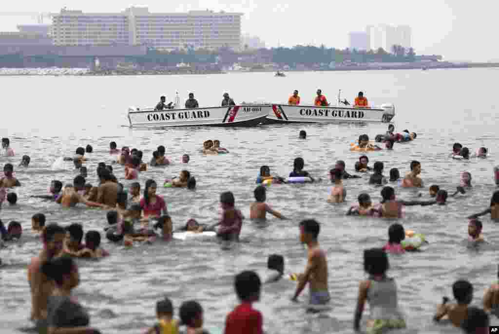 Philippine Coast Guard personnel stay beside people swimming in the polluted waters of Manila's bay, just outside the U.S. Embassy, in the Philippines as they celebrate Easter Sunday, April 20, 2014. Despite a city-imposed swimming ban, many poor Filipino