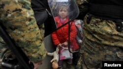A migrant girl holds her toys as Macedonian policemen block migrants at the Greek-Macedonian borders, near the village of Idomeni, Greece Nov. 20, 2015.