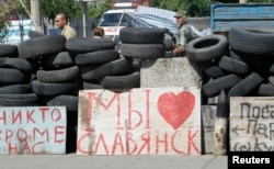 Pro-Russian separatists stand guard at a checkpoint, where a sigh reads "We love Slovyansk," in the eastern city of Slovyansk, Ukraine, July 1, 2014.