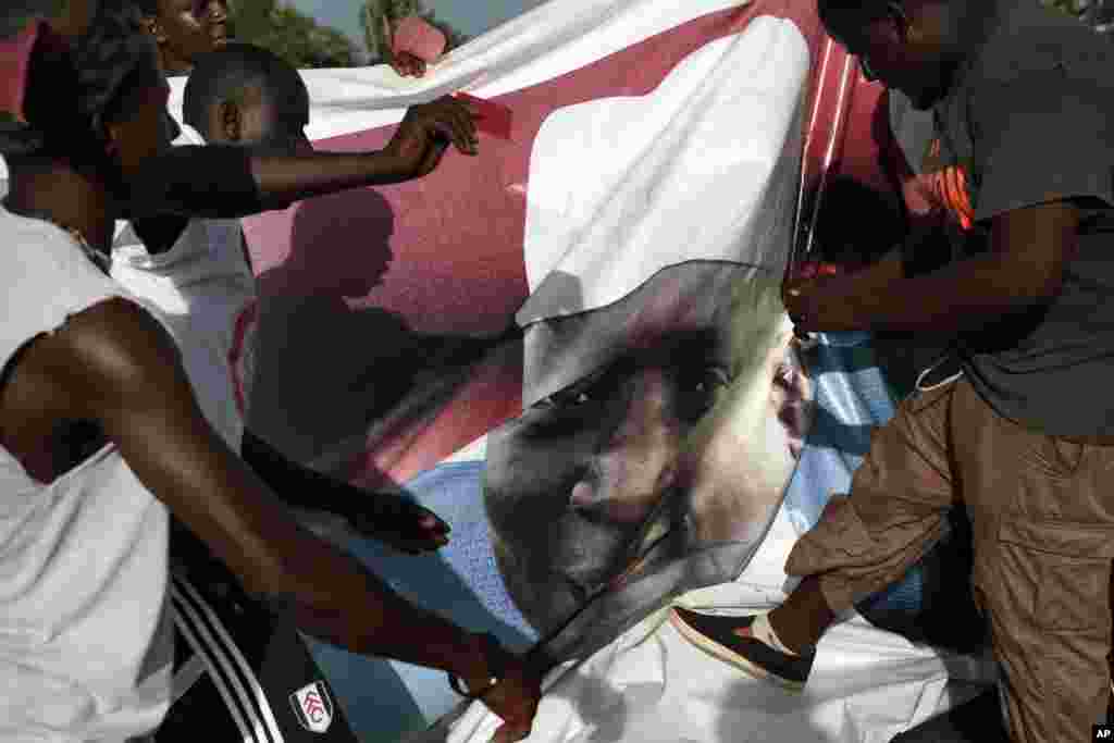 Gambians celebrate the victory of opposition coalition candidate Adama Barrow by tearing down a poster of longtime President Yahya Jammeh in the streets of Serrekunda, Gambia.