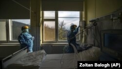 In this March 24, 2020, file photo, medical staff members check a ventilator in protective suits at the care unit for the new COVID-19 infected patients inside the Koranyi National Institute of Pulmonology in Budapest. (Zoltan Balogh/MTI via AP, File)