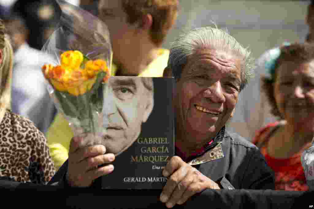 A well-wisher holds flowers and an autobiography of Colombian Nobel laureate Gabriel Garcia Marquez, as he waits outside the Palace of Fine Arts to pay his respects to the beloved author, in Mexico City, April 21, 2014. 