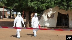 Health workers walk toward an area used for Ebola quarantine after they worked with Fanta Kone, 2, who died of the disease Friday at an Ebola virus center in Kayes, Mali. 