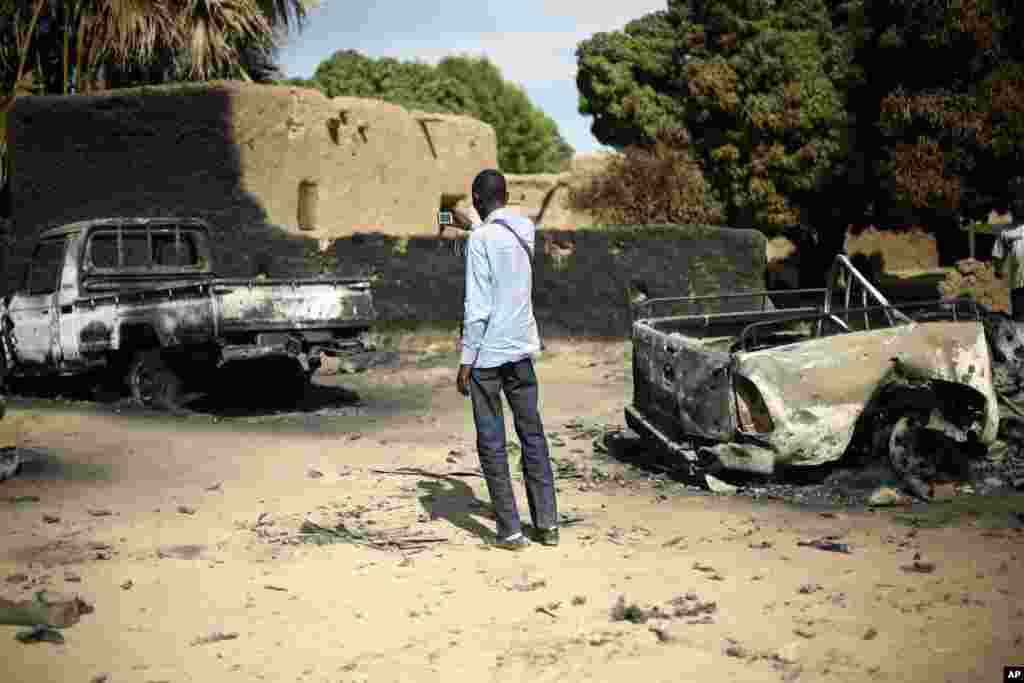 An unidentified man takes a picture of the charred remains of trucks used by radical Islamists on the outskirt of Diabaly, Mali, January 21, 2013. 