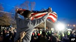 Pristalica Donalda Trampa maše američkom zastavom stojeći naspram grupe demonstranata protiv Trampa za vreme predizborne kampanje 2016, u Betpejdžu u državi Njujork.