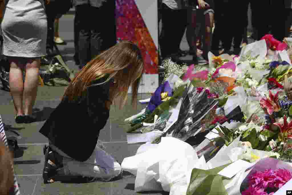 A woman kneels as she lays flowers in a makeshift memorial near the site where a gunman held hostages for 16 hours at a popular Sydney cafe, Australia, Tuesday, Dec. 16, 2014.