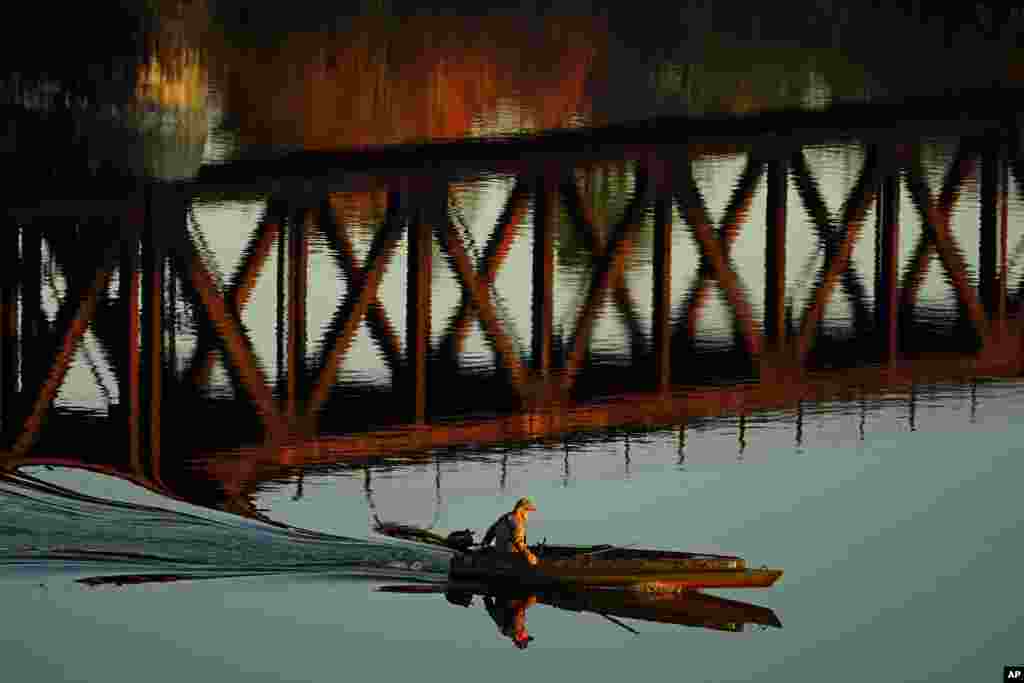 A duck hunter motors by the reflection of a train trestle on the Androscoggin River, Oct. 29, 2021, in Brunswick, Maine.