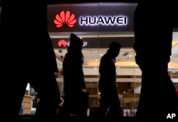 FILE - Pedestrians walk past a Huawei retail shop in Beijing, Dec. 6, 2018.