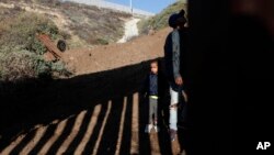 A young Honduran migrant waits for his parents to cross over the U.S. border wall after he was squeezed through one of its gaps, from Playas de Tijuana, Mexico, Dec. 12, 2018.
