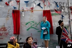 A woman wearing a mask of Queen Elisabeth stands next to the message by the elusive artist Banksy on the anniversary of the Balfour Declaration Bethlehem, West Bank, Nov. 1, 2017. The Balfour Declaration, Britain's promise to Zionists to create a Jewish home in what is now Israel, turns 100 this week.