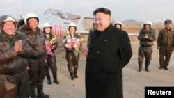 ຜູ້ນຳເກົາຫລີເໜືອ ທ່ານ Kim Jong Un ຢືນຍິ້ມໃນ ຂະນະທີ່ ຢ້ຽມຢາມ ນັກບິນຜູ້ຍິງ.
