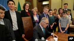Washington Gov. Jay Inslee signs a bill into law at the Capitol in Olympia, Wash., May 21, 2019, that allows licensed facilities to offer "natural organic reduction," which turns a body, mixed with substances such as wood chips and straw, into soil in a s