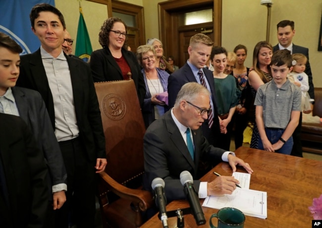 Washington Gov. Jay Inslee signs a bill into law at the Capitol in Olympia, Wash., May 21, 2019, that allows licensed facilities to offer "natural organic reduction," which turns a body, mixed with substances such as wood chips and straw, into soil in a span of several weeks.