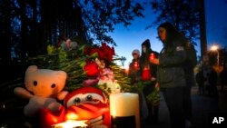 Para mahasiswa menyalakan lilin di antara karangan bunga dan foto-foto korban di luar kampus Universitas Negeri Perm, Rusia, pada 21 September 2021. Tujuh orang tewas dalam peristiwa penembakan di kampus tersebut yang terjaid pada Senin (20/9). (Foto: AP/Dmitri Lovetsky)