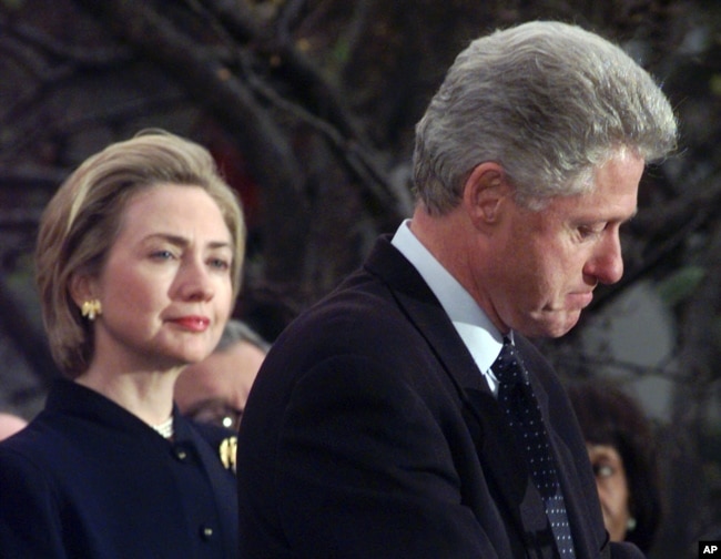 FILE - Then-first lady Hillary Clinton watches her husband, President Bill Clinton, pause as he thanks those Democratic members of the House of Representatives who voted against his impeachment, Dec. 19, 1998.