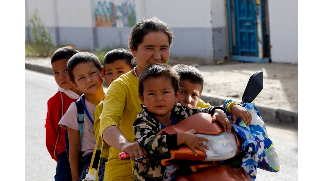 Seorang wanita dan anak-anak Uighur duduk di atas sepeda roda tiga sepulang sekolah di Unity New Village di Hotan, di wilayah Xinjiang, China barat, 20 September 2018. (Foto: AP)