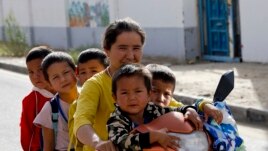 In this Sept. 20, 2018 file photo, a Uighur woman and children sit on a motor-tricycle after school at the Unity New Village in Hotan, in western China's Xinjiang region.