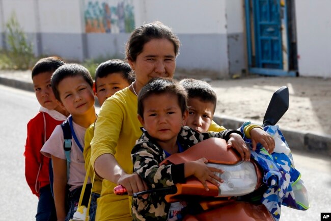 Seorang wanita dan anak-anak Uighur duduk di atas sepeda roda tiga sepulang sekolah di Unity New Village di Hotan, di wilayah Xinjiang, China barat, 20 September 2018. (Foto: AP)