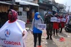 Orang-orang membawa poster untuk mengkampanyekan protokol kesehatan Covid-19 di Bandung, 20 April 2020. (Foto: AFP)