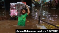 Seorang pedagang mengangkut barang-barangnya melalui air di pasar di daerah yang terkena banjir menyusul hujan lebat di Jakarta, 20 Februari 2021. (Foto: Antara/Muhammad Iqbal via REUTERS