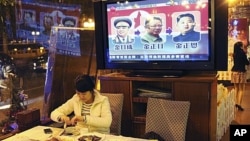 A woman eats a meal in a restaurant in Guangzhou, southern China Guangdong province while television reports on the successive North Korean leaders; from left Kim Il Sung, Kim Jong Il and Kim Jong Un, December 20, 2011.