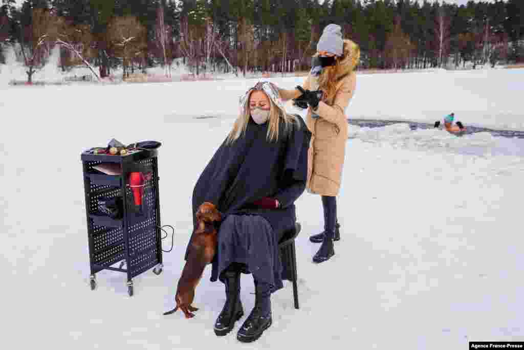 A hairdresser cuts hair on the frozen lake Babelitis while a winter swimmer enjoy swimming in an ice hole, Feb. 15, 2021, in Riga, Latvia, during the COVID-19 pandemic.
