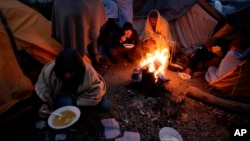 Migrants eat around a fire at a camp in Velika Kladusa, Bosnia, close to the border to Croatia, Nov. 18, 2018. 