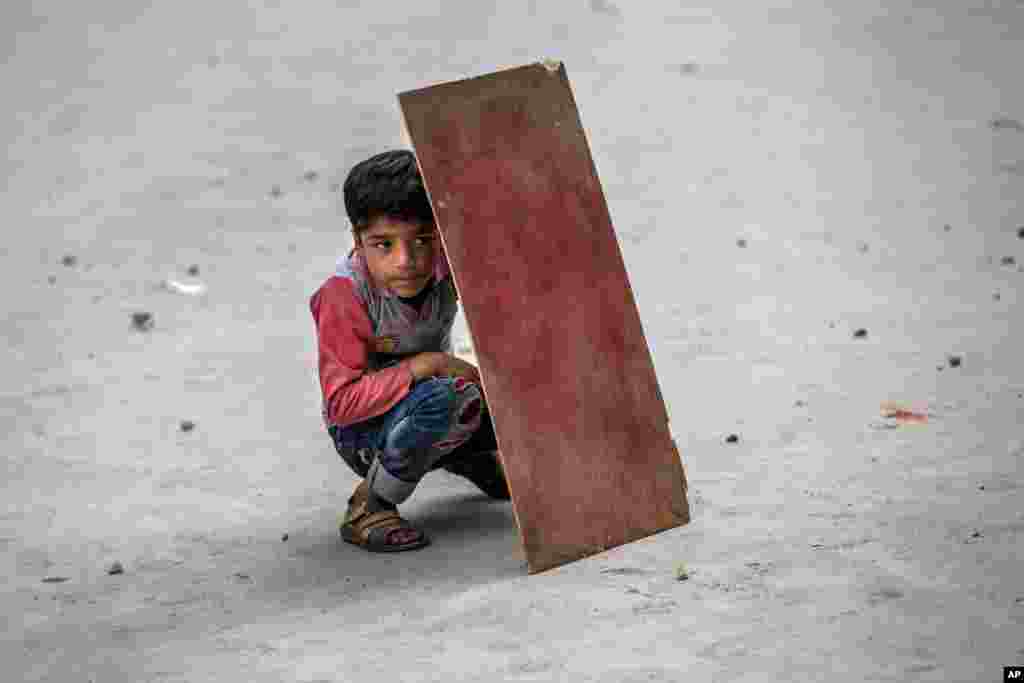 A Kashmiri boy shields himself with plywood from stones and glass marbles during a clash between Indian policemen and protesters during a protest in Srinagar, Indian controlled Kashmir.