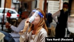 Seorang pelanggan perempuan yang mengenakan pelindung wajah, meminum kopi di sebuah kafe di Roma saat Italia mulai mengendorkan karantina Covid-19. 