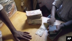FILE - A Mogadishu money changer checks a U.S. $100 bill with a counterfeit detection device in a market in the city in Mogadishu, Dec. 8, 1992.