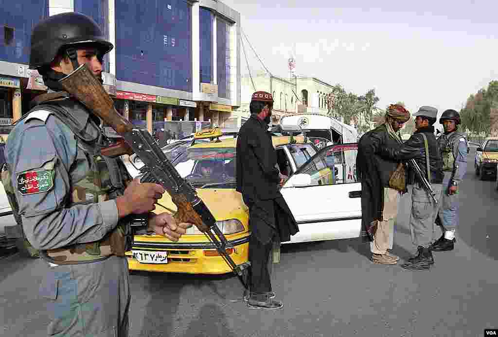 An Afghan policeman, left, stands guard as a colleague, right, searches a taxi passenger at a police checkpoint following the killing of civilians by a U.S. soldier in Kandahar province, March. 12, 2012. (AP)
