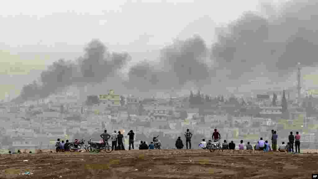People on a hilltop watch smoke rising from a fire caused by a strike in Kobani, Syria, during fighting between Syrian Kurds and the militants of Islamic State group, on the outskirts of Suruc, at the Turkey-Syria border, Oct. 11, 2014. 