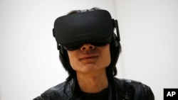 FILE - Peijun Guo wears the Oculus Rift VR headset at the Oculus booth at CES International in Las Vegas, Jan. 6, 2016. Facebook CEO Mark Zuckerberg seems to be realizing that the headsets his company's Oculus division has been making are too expensive and confining to appeal to the masses.