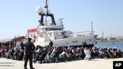 Des immigrants assis à terre après le débarquement du navire d'aide de la station migrant «Phoenix» dans le port d'Augusta, en Sicile, au sud de l'Italie, samedi 9 mai 2015.